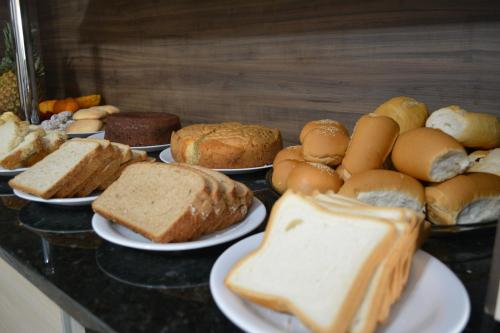 a bunch of different types of bread on plates on a counter at Hotel Consalter in Rodeio Bonito
