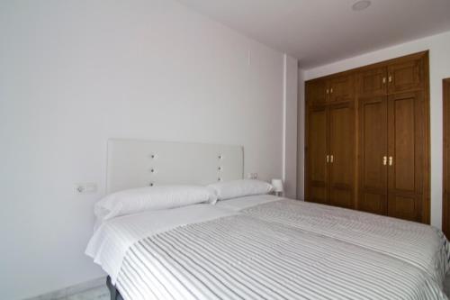 a white bed in a white bedroom with wooden cabinets at Apartamentos Centro 1 El Puerto de Santa Maria in El Puerto de Santa María