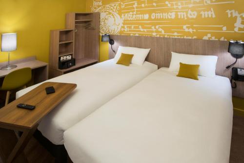 two beds in a hotel room with a desk and a table at ibis Styles Carcassonne La Cité in Carcassonne