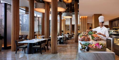 a chef preparing food in a restaurant with tables at Hyatt Regency Changchun in Changchun