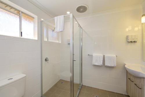 a white bathroom with a shower and a sink at Smart Motels Bert Hinkler in Bundaberg