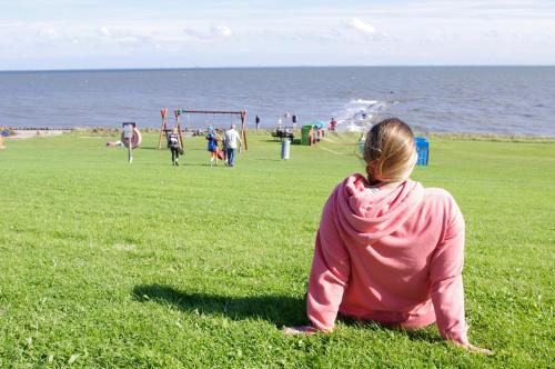 a woman sitting on the grass looking at the beach at Wiesenblick in Pellworm