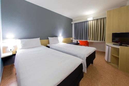 a hotel room with two beds and a flat screen tv at ibis Araçatuba in Araçatuba