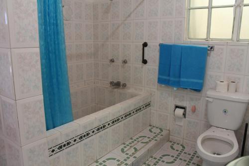 a bathroom with a tub and a toilet and a blue shower curtain at Condominio AcaGutty 1B in Acapulco