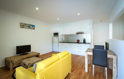 a living room with a yellow couch and a kitchen at Pelicans Albany Middleton Beach in Albany