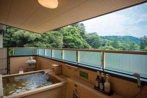 a balcony with a tub with a view of trees at Tachibana Shikitei in Kaga