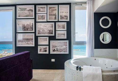 ein Badezimmer mit einer großen Badewanne und Bildern an der Wand in der Unterkunft Tal By The Beach - An Atlas Boutique Hotel in Tel Aviv