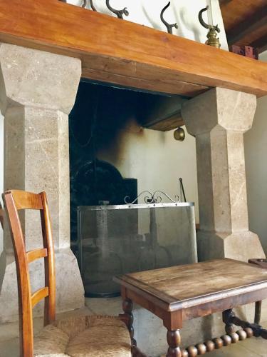 une cheminée en pierre avec une table en bois et une télévision dans l'établissement La Petite Maison des Artistes, à Castelnau-Pégayrols