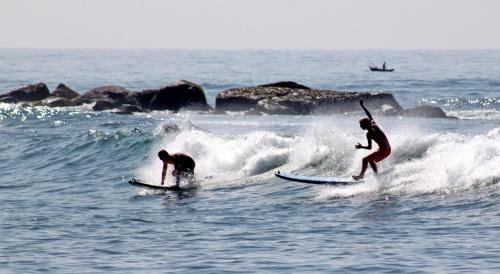 two men riding a wave on surfboards in the ocean at Sun & Tree HomeStay (With Green Nature View) in Mirissa