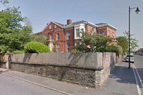 a brick house with a fence in front of a street at Queens Guesthouse Manchester in Manchester
