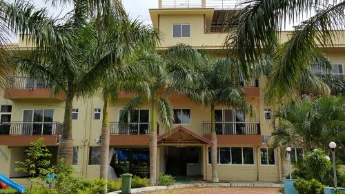 a building with palm trees in front of it at Anand Agro Tourism Kashid in Alibaug