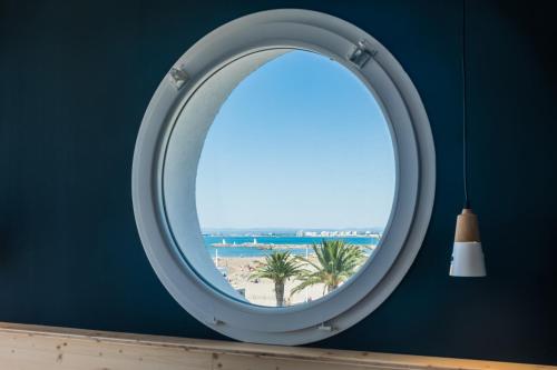 a round mirror in a blue wall with a view of the beach at Hôtel Café Miramar in Le Grau-du-Roi