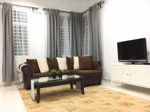 a living room with a brown couch and a tv at Ceri Merah Homestay in Kuantan