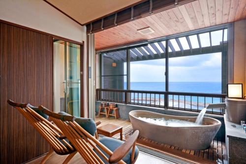 ein Bad mit einer Badewanne und einen Balkon mit Stühlen in der Unterkunft Hotel Sanrakuso in Shirahama