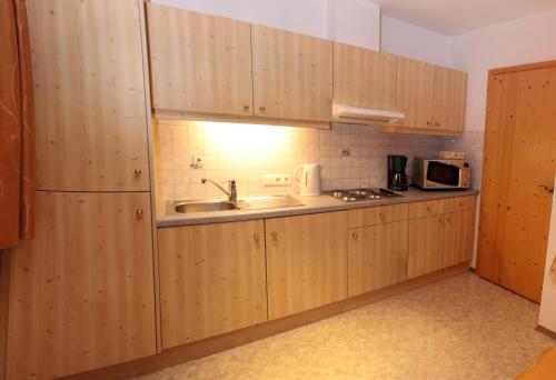 cocina con armarios de madera, fregadero y microondas en Haus Ferienglück, en Neustift im Stubaital