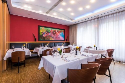 a restaurant with white tables and chairs and a red wall at SEEhotel Friedrichshafen in Friedrichshafen