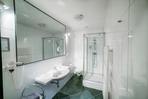 a white bathroom with a sink and a shower at Stadthotel Kramer in Villach