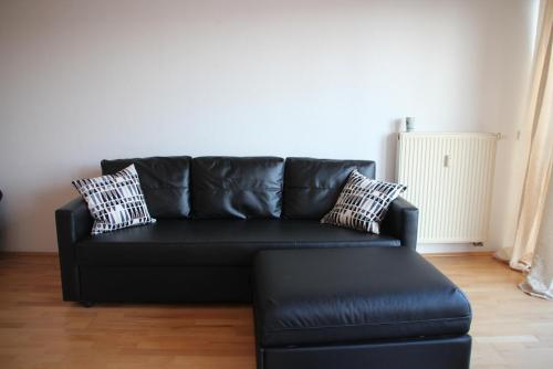 un sofá de cuero negro en una sala de estar con taburete en Apartment am Fluss/Park en Leipzig