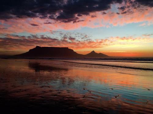 a sunset on the beach with a mountain in the background at Atlantic Breeze in Cape Town