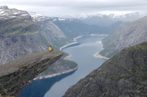 a person sitting on top of a cliff overlooking a river at Trolltunga Studios in Odda