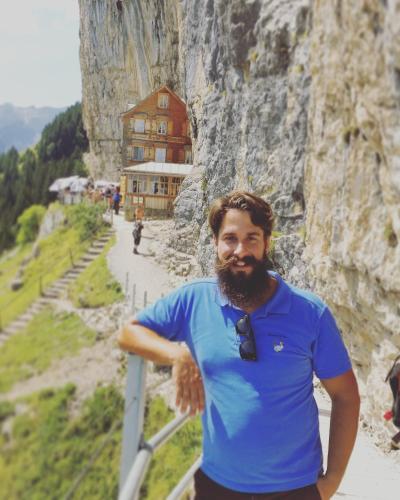 a man in a blue shirt and tie standing next to a mountain at Ferienhaus Alpenpanorama Chalet in Mollenberg