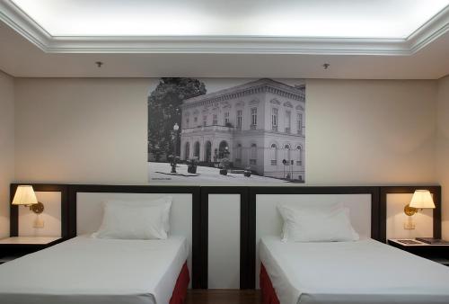 two beds in a room with a picture of the white house at Master Grande Hotel - Próximo ao Palácio do Governo in Porto Alegre