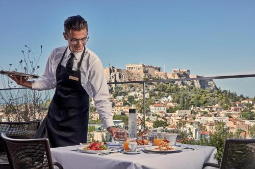 a man standing in front of a table with food at Electra Metropolis in Athens
