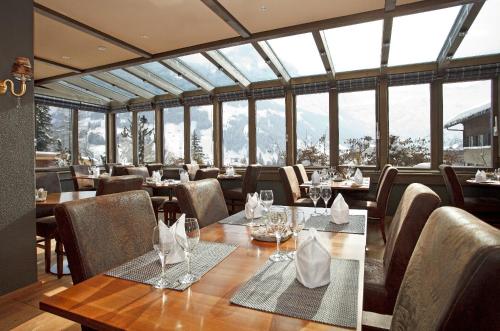 a dining room with tables and chairs and windows at Hotel Steinmattli in Adelboden