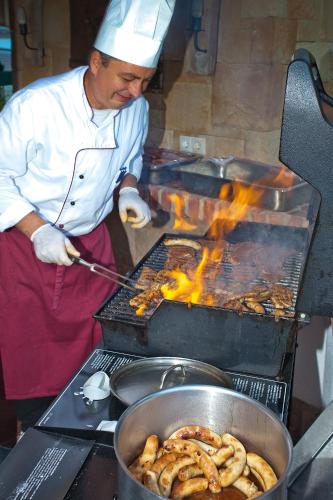 a man cooking food on a grill with flames at Landhotel Alpenhof Filzmoos in Filzmoos