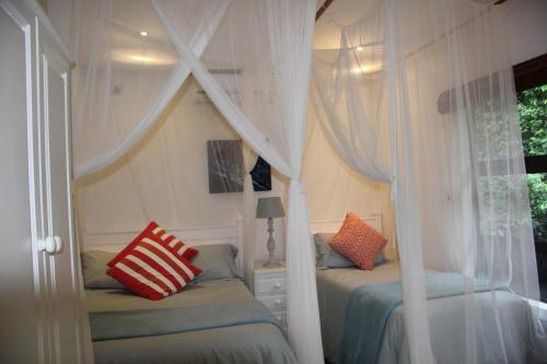 a bedroom with two beds with white curtains and a window at Campismo Ninho 40 in Ponta Malangane