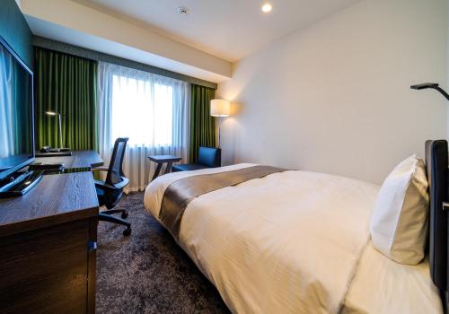 a hotel room with a bed and a desk and a television at Daiwa Roynet Hotel Koriyama Ekimae in Koriyama