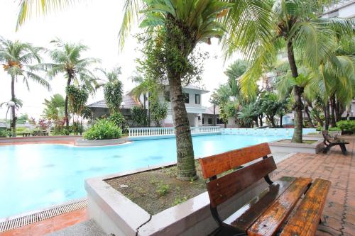 a wooden bench next to a swimming pool with palm trees at Vista Horizon Melaka in Melaka