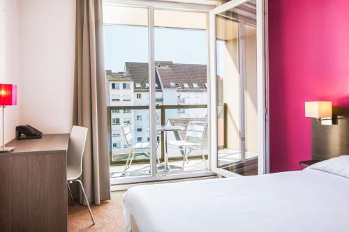 ストラスブールにあるアパートホテル アダージョ アクセス ストラスブール プティット フランスのベッドと大きな窓が備わるホテルルームです。