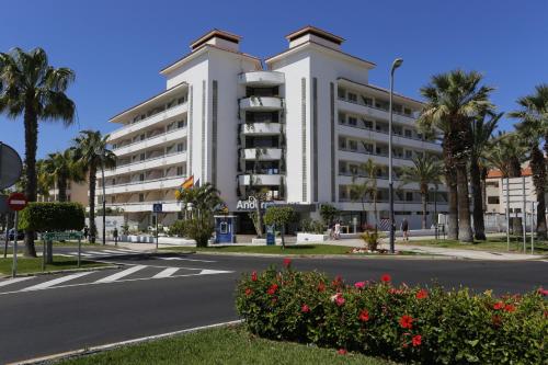 a white building with palm trees and a street at Hotel-Apartamentos Andorra in Playa de las Americas