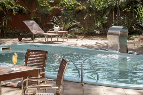 uma piscina com cadeiras, uma mesa e uma fonte em Intercity Porto Alegre Aeroporto em Porto Alegre