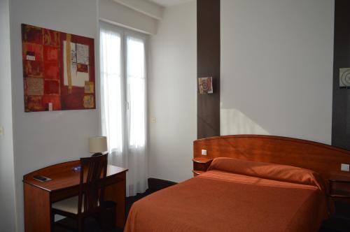 a bedroom with a bed and a desk and a window at Hotel de La Paix in Oloron-Sainte-Marie