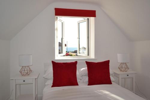 a white bed with red pillows and a window at South Coast Haven Apartments in Peacehaven