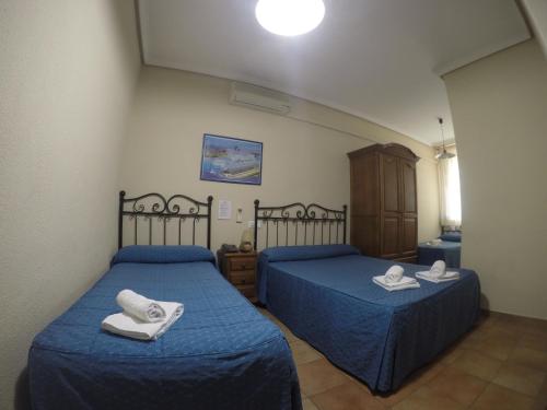 two beds in a room with blue sheets and towels at Hostal El Pilar in Madrid