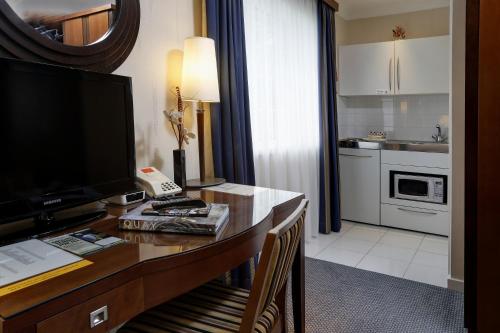 a room with a desk with a television and a kitchen at Best Western Homestead Court Hotel in Welwyn Garden City