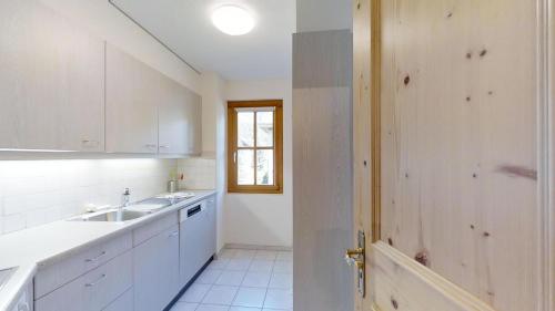 a kitchen with white cabinets and a sink and a door at La Planüra 15 in Maloja