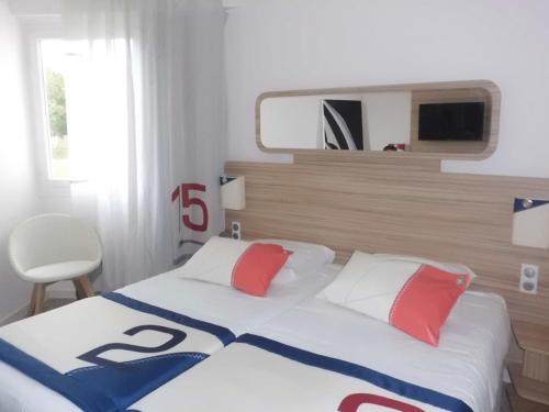 a bedroom with a white bed with red and blue pillows at Hotel Club Le Plein Sud Vacances Bleues in Hyères