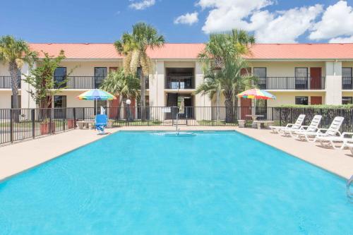 a swimming pool with chairs and umbrellas in front of a building at Days Inn & Suites by Wyndham Navarre - near Beaches Hurlburt in Navarre