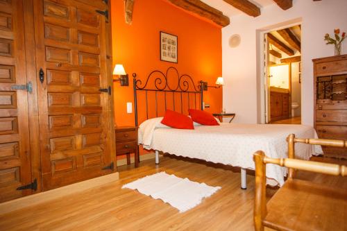 ペドラサにあるEl Bulín de Pedraza - Casa del Serradorのオレンジ色の壁のベッドルーム1室、赤い枕付きのベッド1台が備わります。