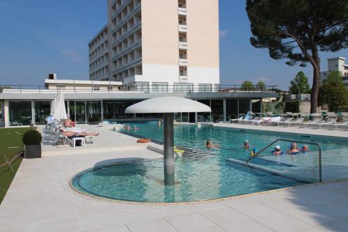 a swimming pool with an umbrella and people in it at Hotel Smeraldo in Abano Terme