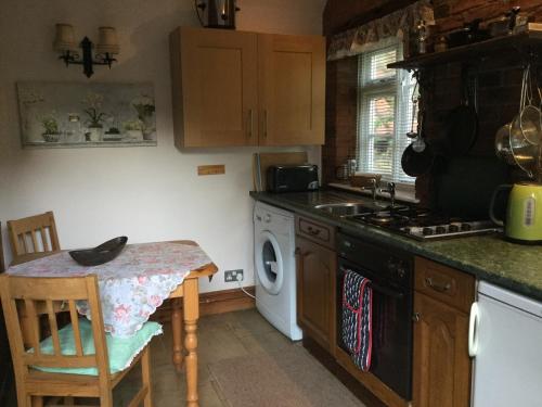 a kitchen with a stove and a sink and a table at Moat Cottage Barns in Corby