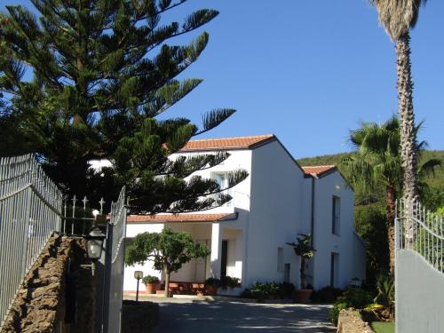 a white house with palm trees and a fence at Arenosu Comfort Country Guesthouse in Fertilia