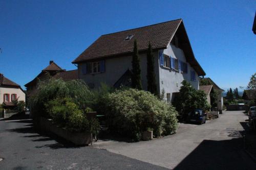 a white house with a brown roof and some bushes at Appartement Les Iris in Bevaix