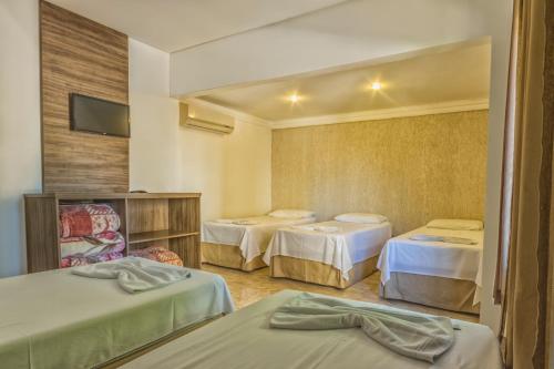 a hotel room with three beds and a tv at Hotel Holiday Foz in Foz do Iguaçu