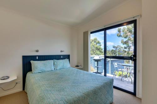 a bedroom with a bed and a balcony with a view at Port Huon Cottages in Port Huon