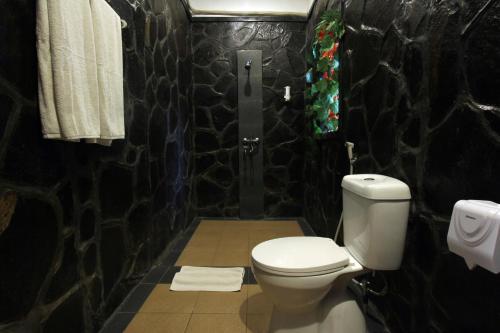 a bathroom with a toilet and a black stone wall at Nara Ubud Cottage by Mahaputra in Ubud